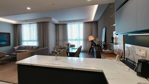 Une chambre d’hôtel moderne dotée d’un îlot de cuisine en marbre, d’un coin repas avec une table et des chaises, d’un canapé et d’un téléviseur à écran plat fixé au mur.