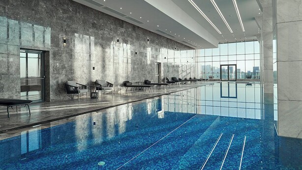 Une piscine intérieure moderne, de forme longue et étroite, avec des sièges disposés le long des bords et une grande fenêtre offrant une vue sur le paysage urbain.