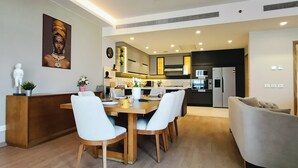 Une cuisine moderne dotée d’appareils électroménagers intégrés, un coin repas avec une table en bois et des chaises blanches, et un salon avec un canapé.