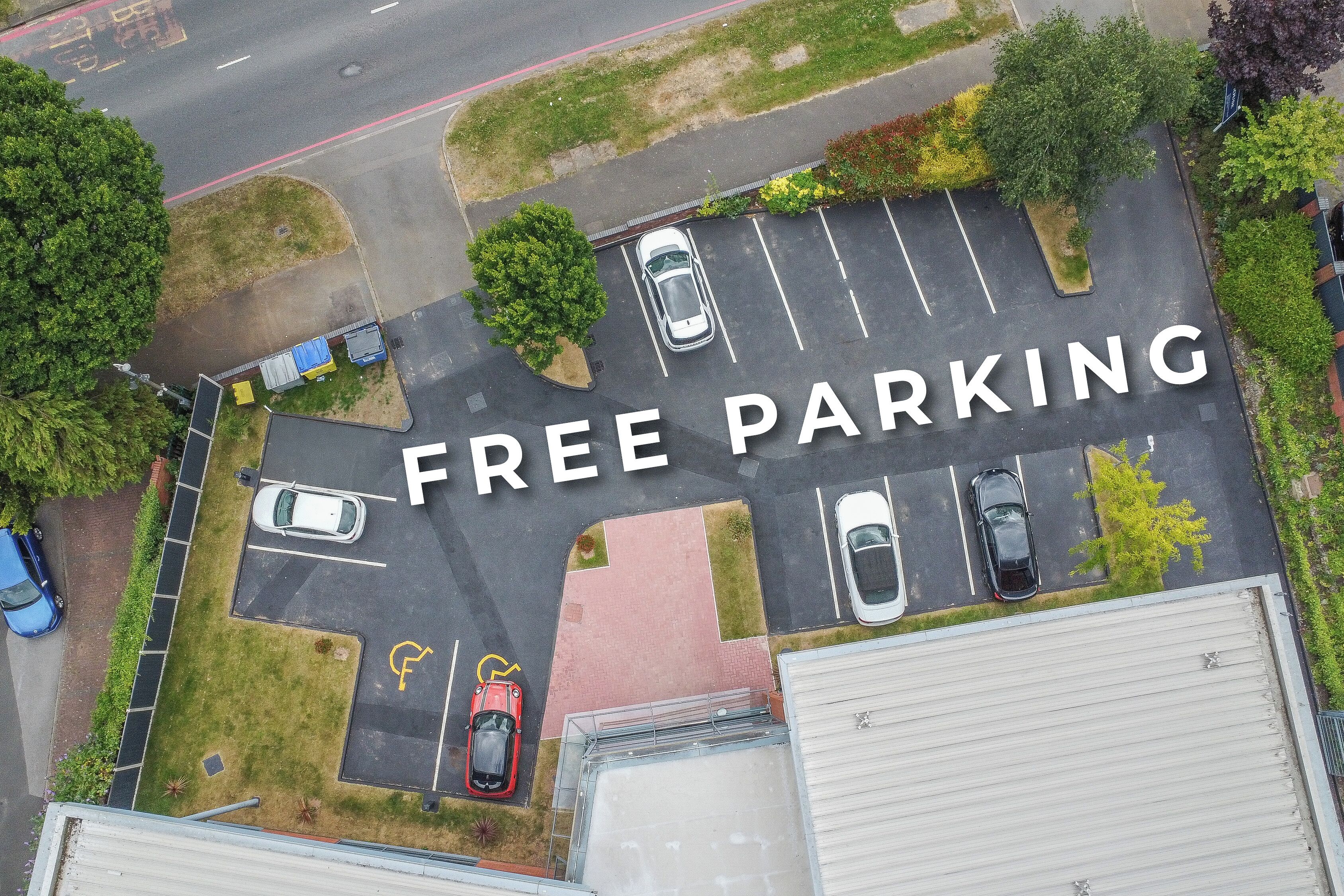 Luftaufnahme eines Parkplatzes mit der Beschilderung 'FREE PARKING', mehreren Autos und umgebender Bepflanzung.