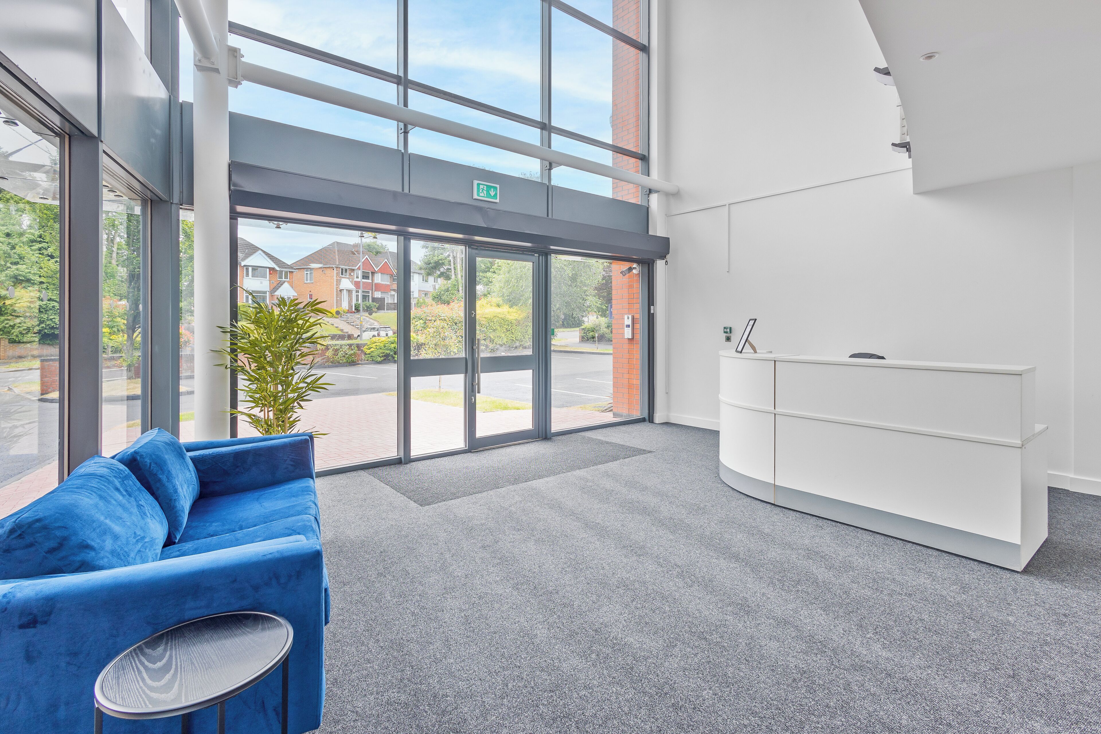 Eine moderne Lobby mit einem blauen Sofa, einem Empfangstresen und großen Fenstern mit Blick ins Freie.