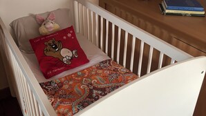 A crib with a patterned blanket, a red pillow with a bear design, and a wooden nightstand with books. - Charming house 3 suites/terrace/garden 6 persons (Moulins)