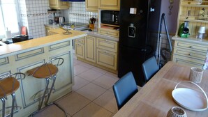 A kitchen with a central island, bar stools, a refrigerator, and a microwave. - Charming house 3 suites/terrace/garden 6 persons (Moulins)