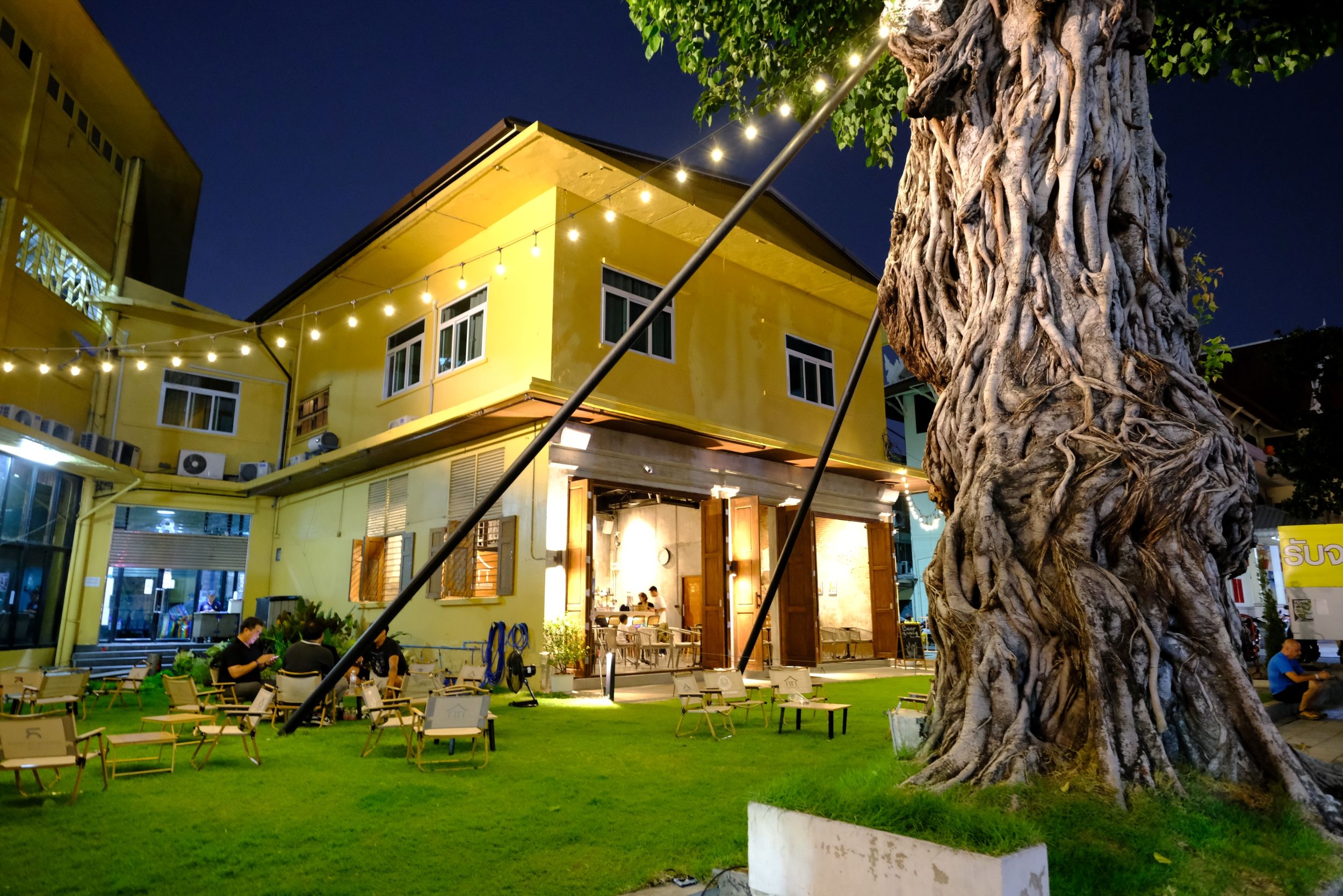 A yellow building with outdoor seating and a large tree.