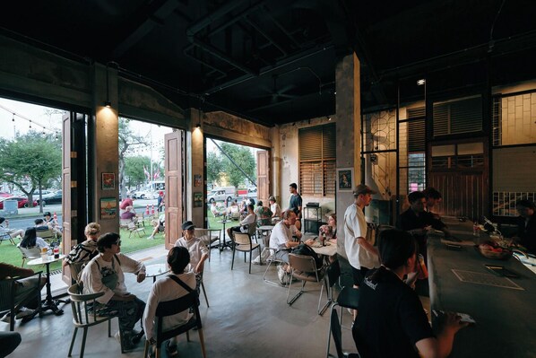 An indoor dining area with tables and chairs, large windows, and a view of the street outside. - Kosin House (Bangkok)