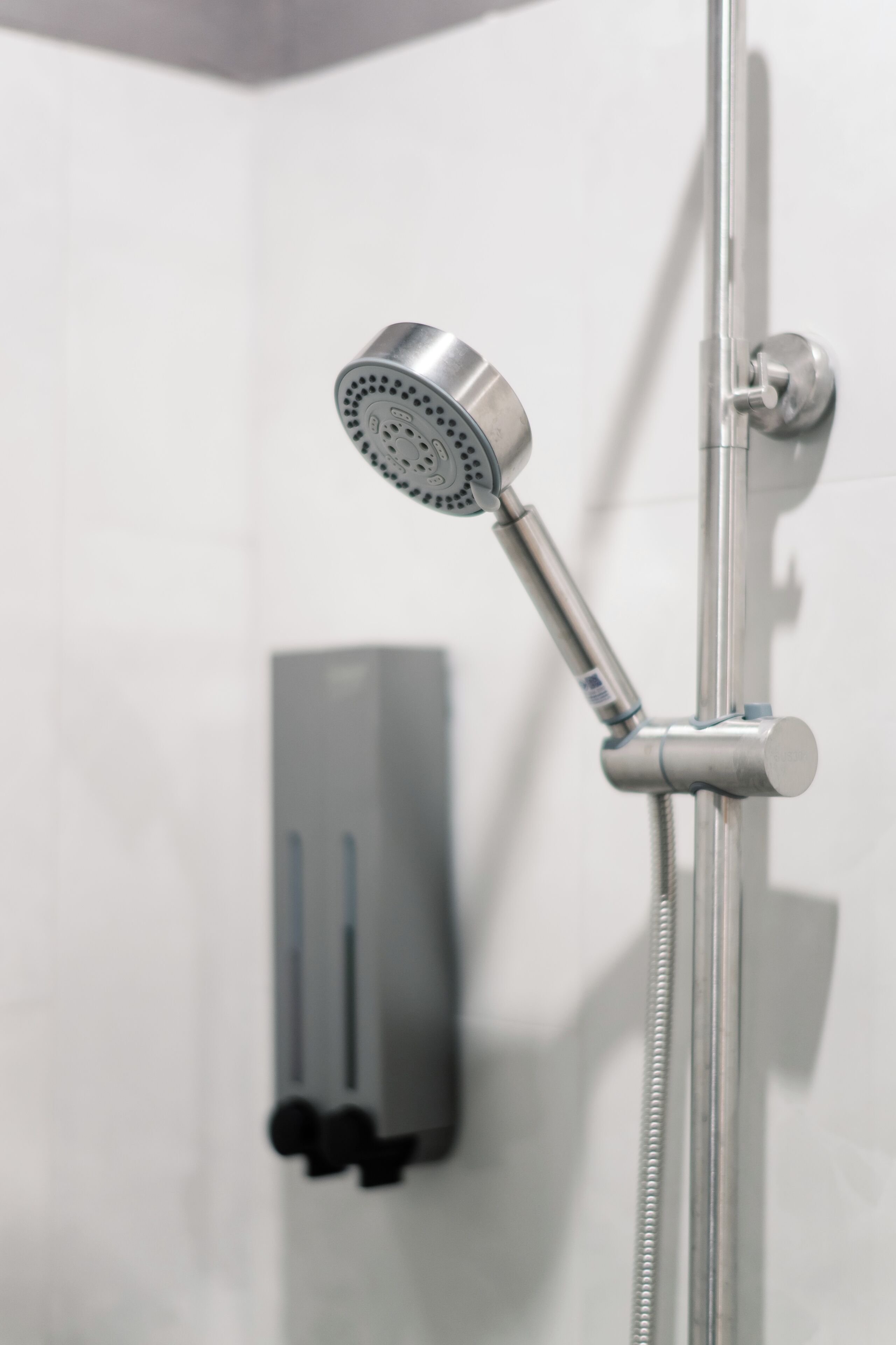 A showerhead with a flexible hose, a wall-mounted soap dispenser, and a towel rack.