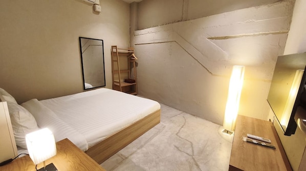 Une chambre d’hôtel comprenant un lit, une table de chevet, une lampe, un miroir et une étagère en bois.