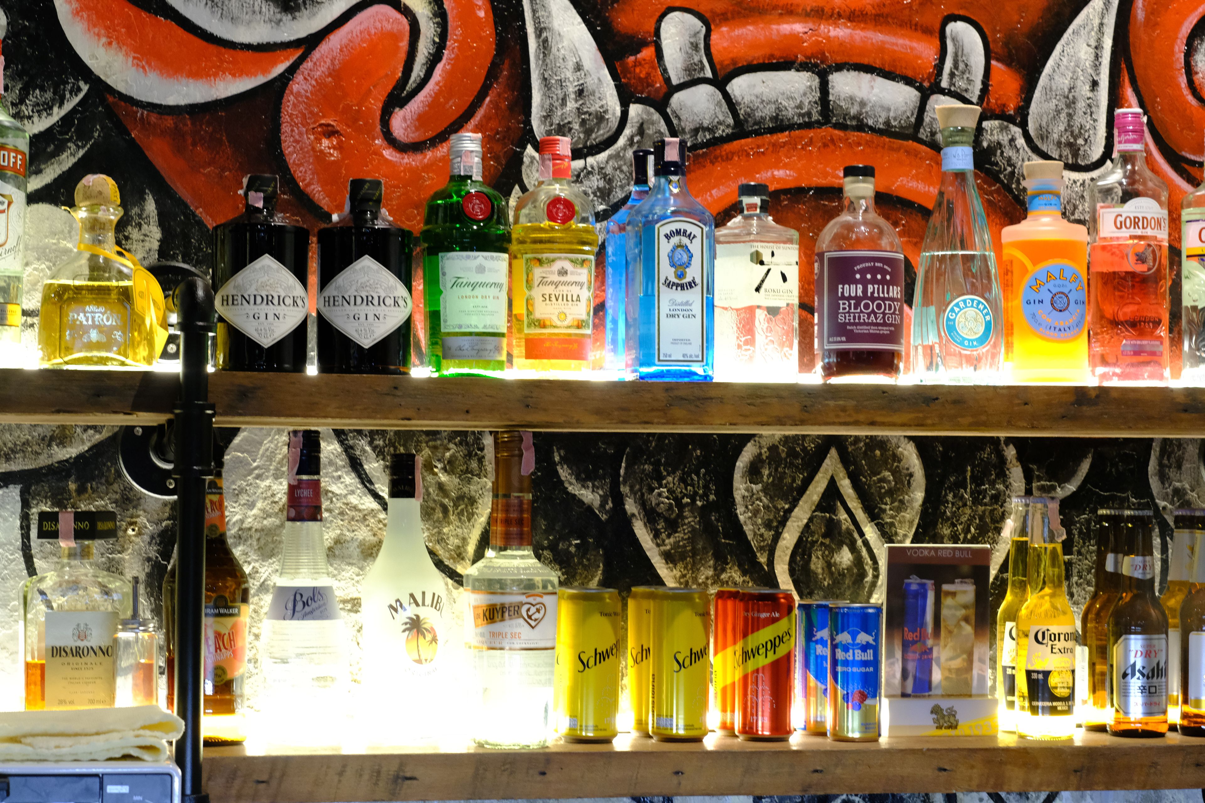 Diverses ampolles de licor exposades a prestatges davant d'un mur amb un mural.