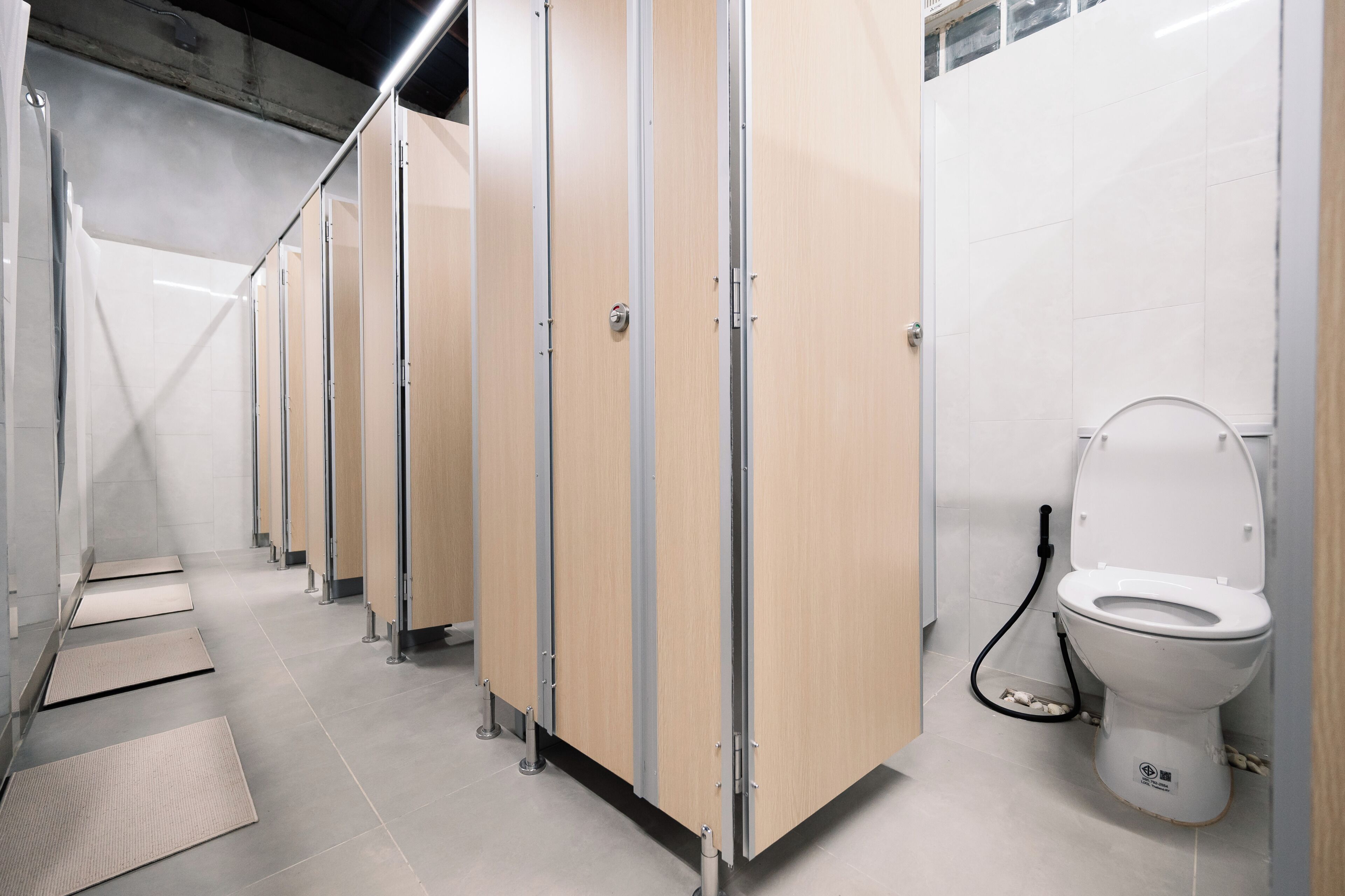 A row of wooden stalls with a white tiled floor, a visible toilet, and a metal handrail.