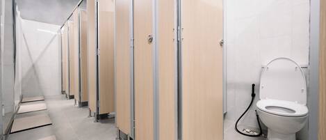 A row of wooden stalls with a white tiled floor, a visible toilet, and a metal handrail.
