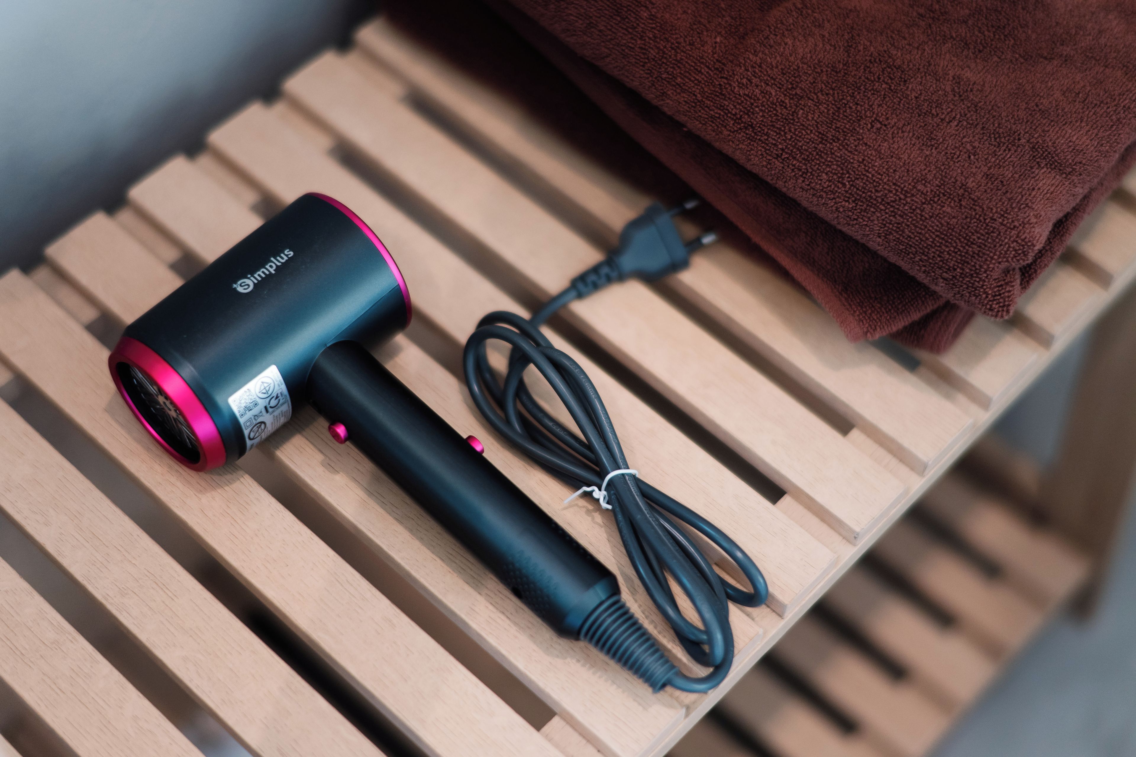 A portable hair dryer with a cord and a power adapter on a wooden surface.