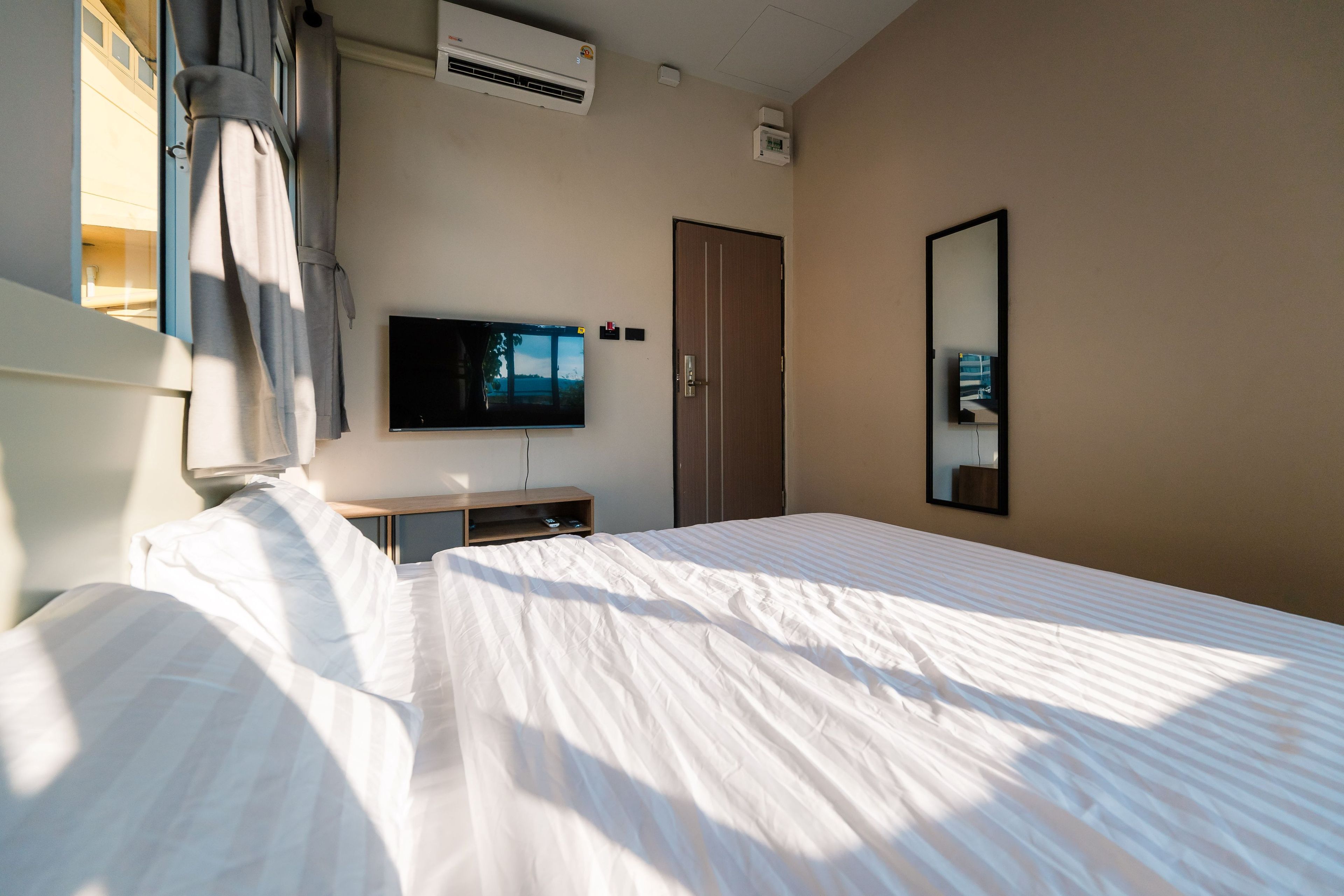 A hotel room with a bed, a flat-screen TV mounted on the wall, a wardrobe, and a window with curtains.