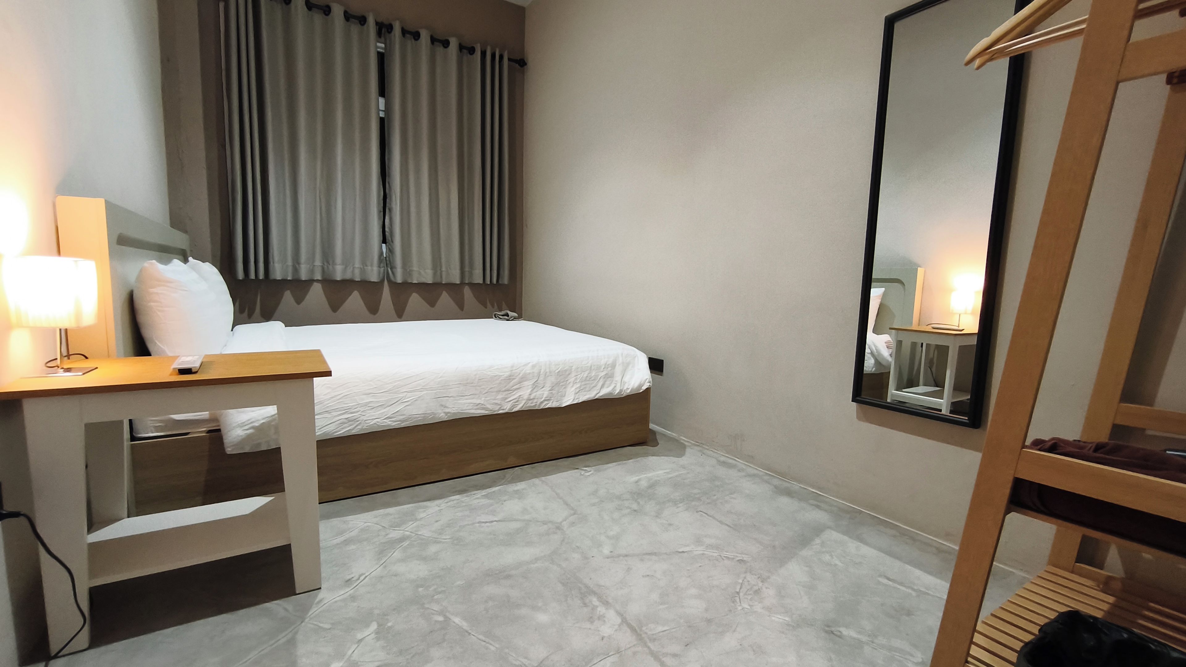 A hotel room with a bed, bedside table, lamp, and a mirror.