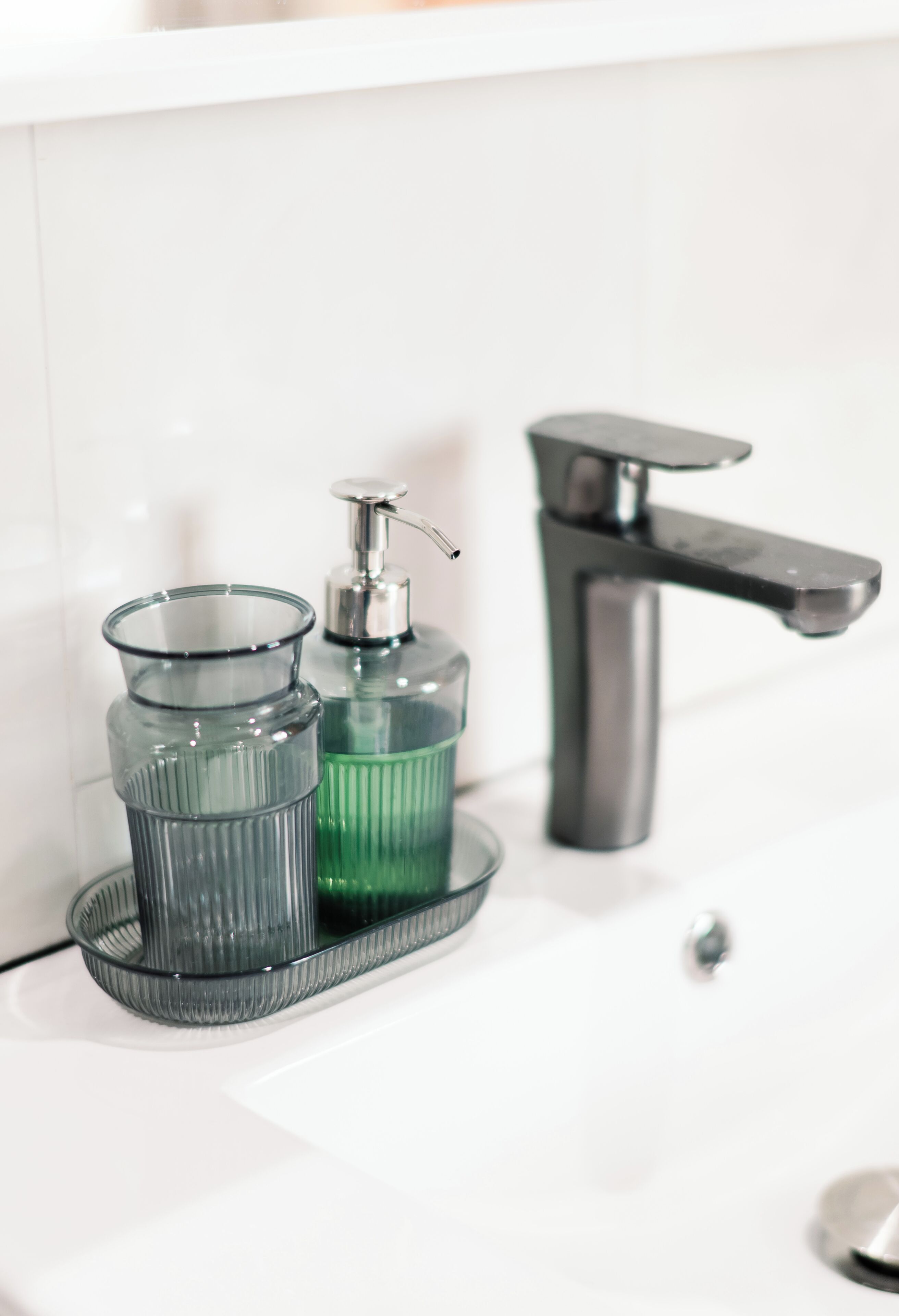 A bathroom sink with a modern faucet and two glass containers on a tray.