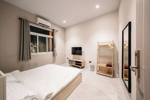 A modern hotel room with a bed, TV, air conditioning unit, and a wooden wardrobe. - Kosin House (Bangkok)