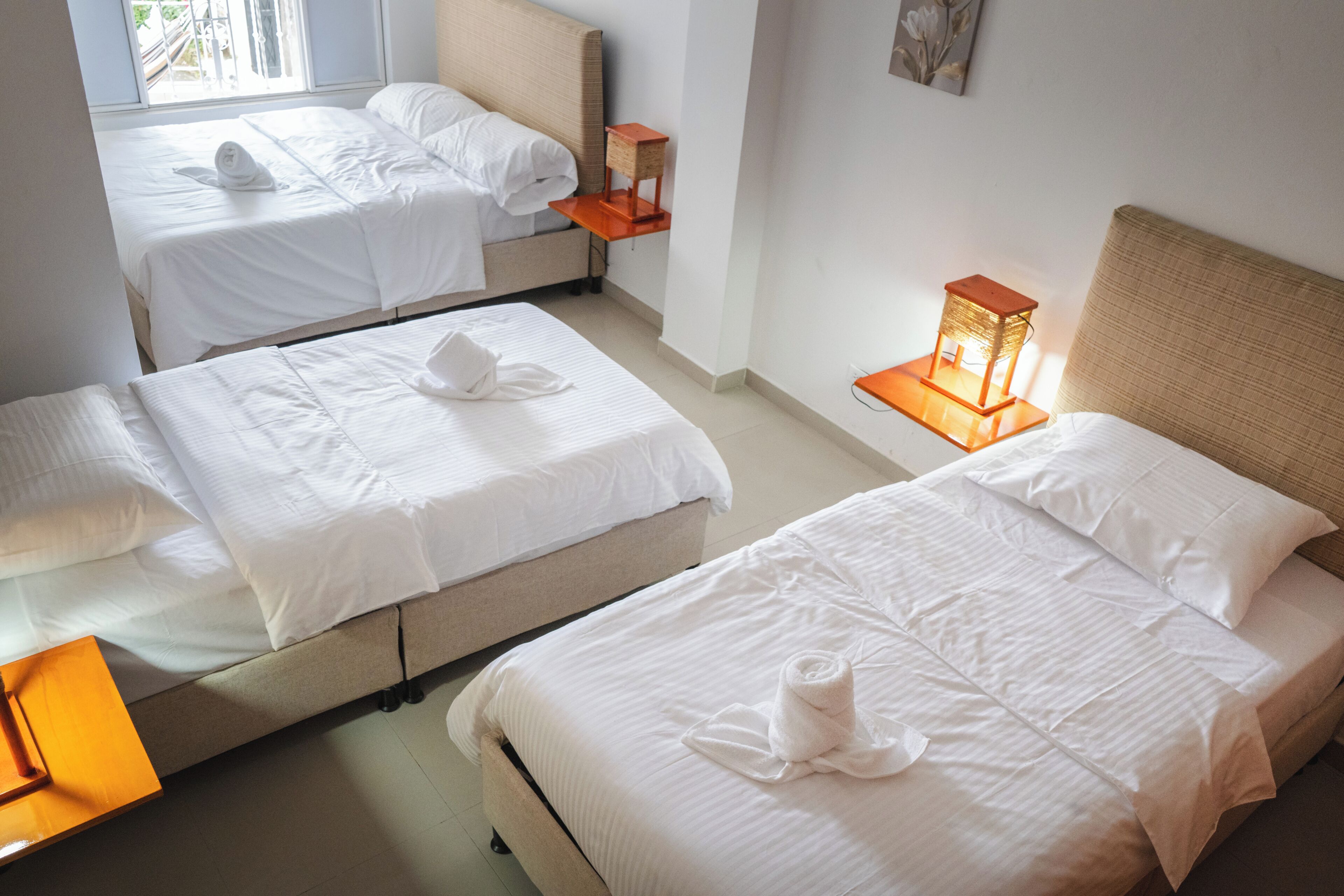 A hotel room with two beds, a nightstand with a lamp, and a window with a view.