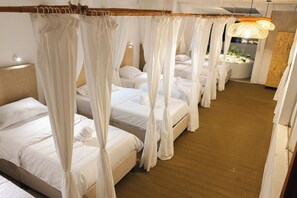 A hotel room with four beds, each with a canopy, a small indoor garden, and a wooden floor.