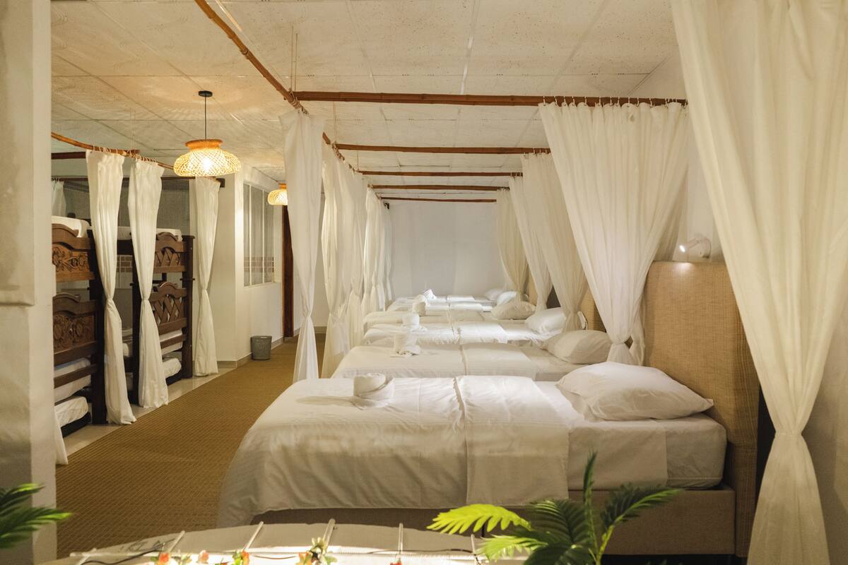 Una habitación de hotel con varias camas, ropa de cama blanca y techo de madera.