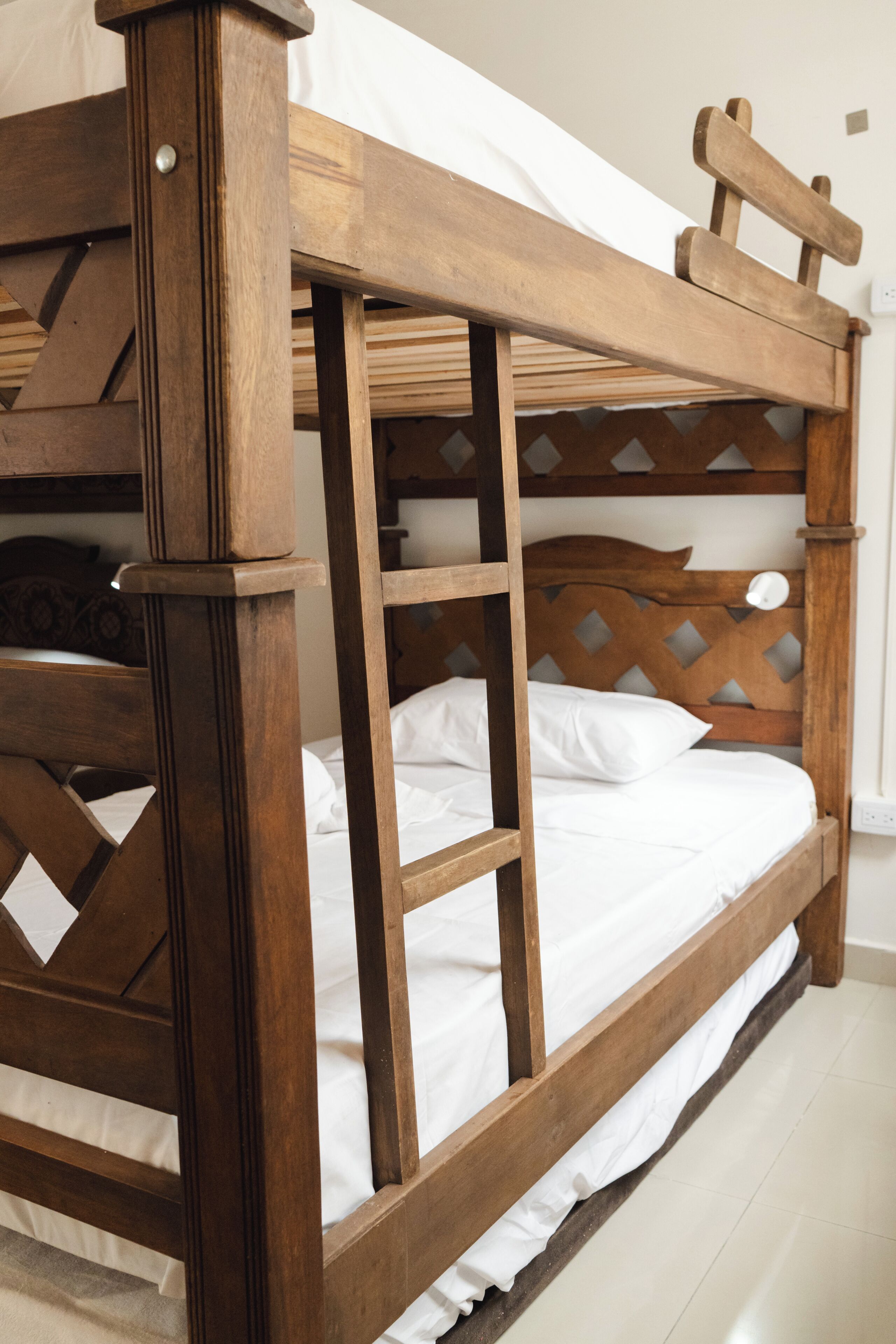 A wooden bunk bed with a ladder, white bedding, and a headboard with a diamond pattern.