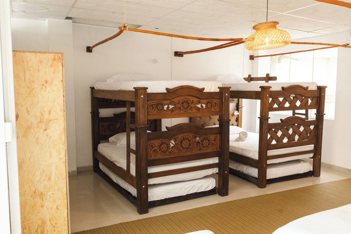 Una habitación con dos camas literas de madera, una lámpara de techo tejida y una puerta de madera.