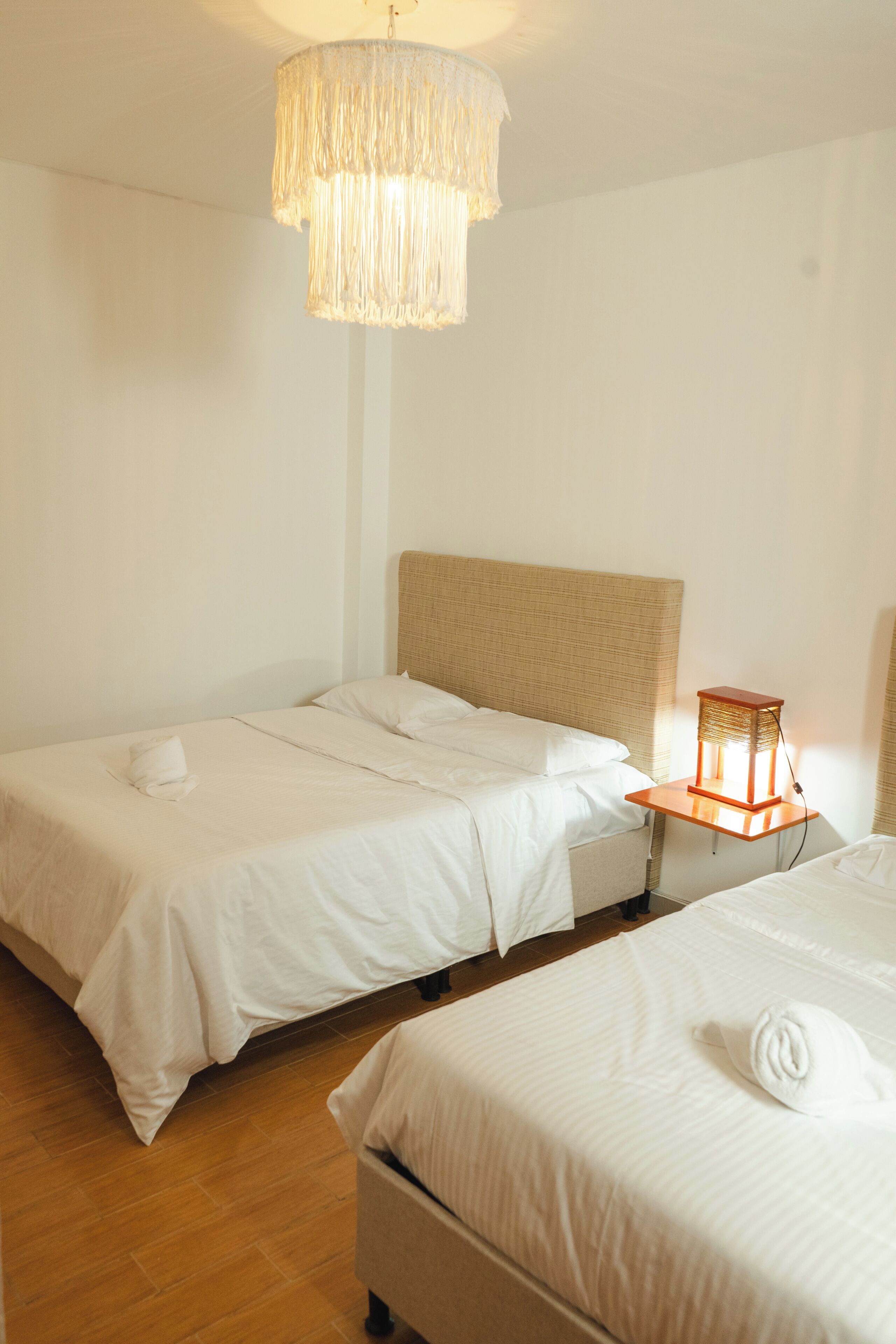 A hotel room with two beds, a hanging light fixture, and a bedside table with a lamp.