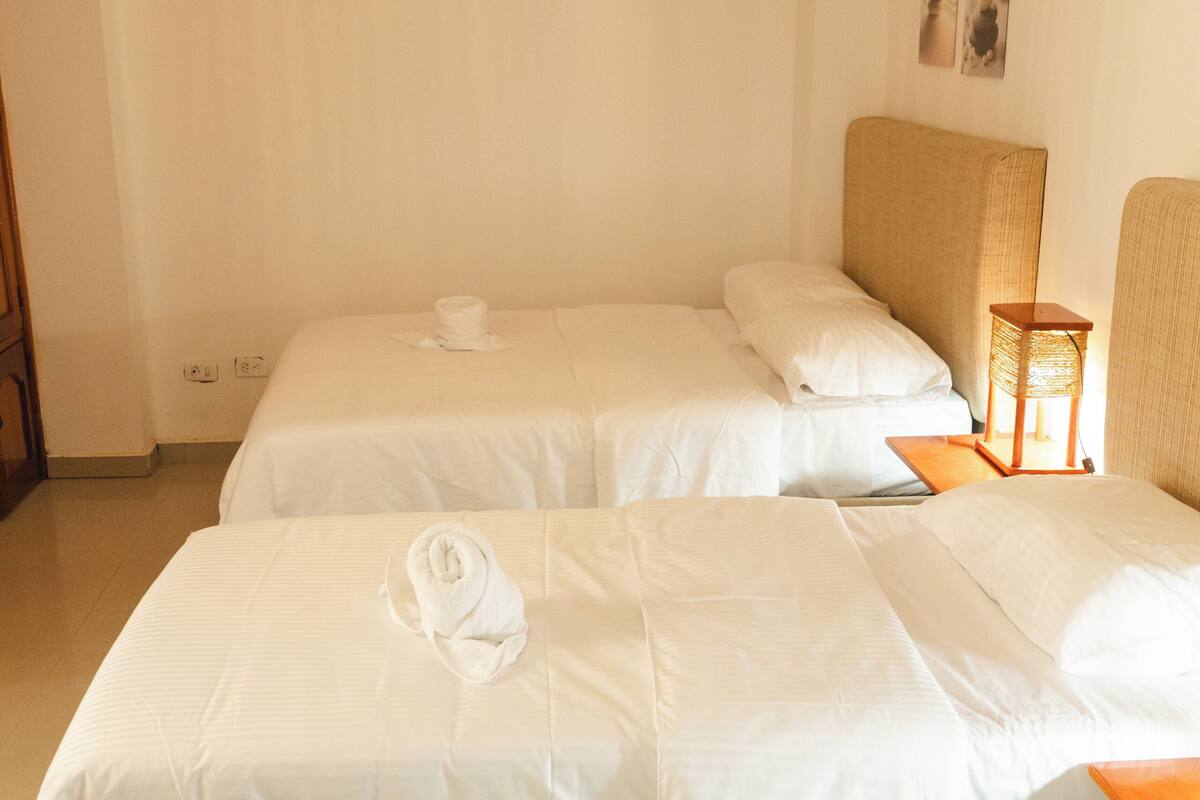 Habitación de hotel con dos camas, una mesita de noche, una lámpara y un cuadro colgado en la pared.