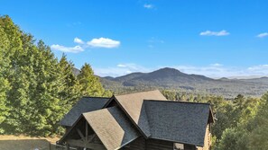 A cabin with a sloped roof, surrounded by dense forest and a mountain in the background. - Stunning Mountain Views & Sunsets, Hot Tub + Fire Pit,  4BR Blue Ridge Retreat (Nebo)