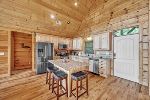 A wooden cabin interior with a kitchen featuring a granite island, bar stools, stainless steel appliances, and a white door. - Stunning Mountain Views & Sunsets, Hot Tub + Fire Pit,  4BR Blue Ridge Retreat (Nebo)