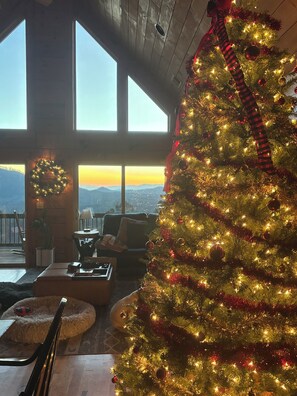 A Christmas tree decorated with lights and ornaments, a fireplace, a view of the mountains, and a cozy seating area with a lamp and a plant. - Stunning Mountain Views & Sunsets, Hot Tub + Fire Pit,  4BR Blue Ridge Retreat (Nebo)