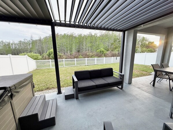 An outdoor patio with a built-in grill, a cushioned seating area, and a view of a grassy yard.