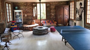 A room with a ping pong table, a bookshelf, a round table, and a sofa. - Gîte le Moulin Fontaine (Saint-Martin-le-Gaillard)