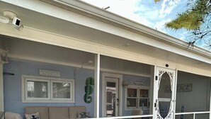 A covered porch with outdoor seating, a door labeled 'COTTAGE,' and a window with a decorative seahorse.