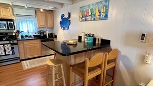 A kitchen with wooden cabinets, a black countertop, a ceiling fan, and a painting of sailboats on the wall.