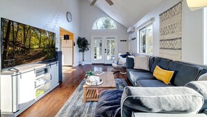 Tilava olohuone, jossa on suuri taulutelevisio, kattotuuletin, puinen sohvapöytä ja tyynyillä varustettu sohva.