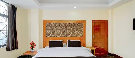 A hotel room with a large bed, a wooden headboard, a small table with a vase of flowers, and a red door.