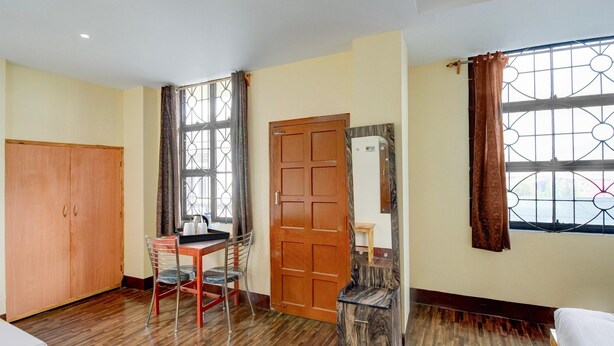 Una habitación con un armario de madera, un escritorio con silla, una cama, un ventanal con cortinas y un espejo en la pared.