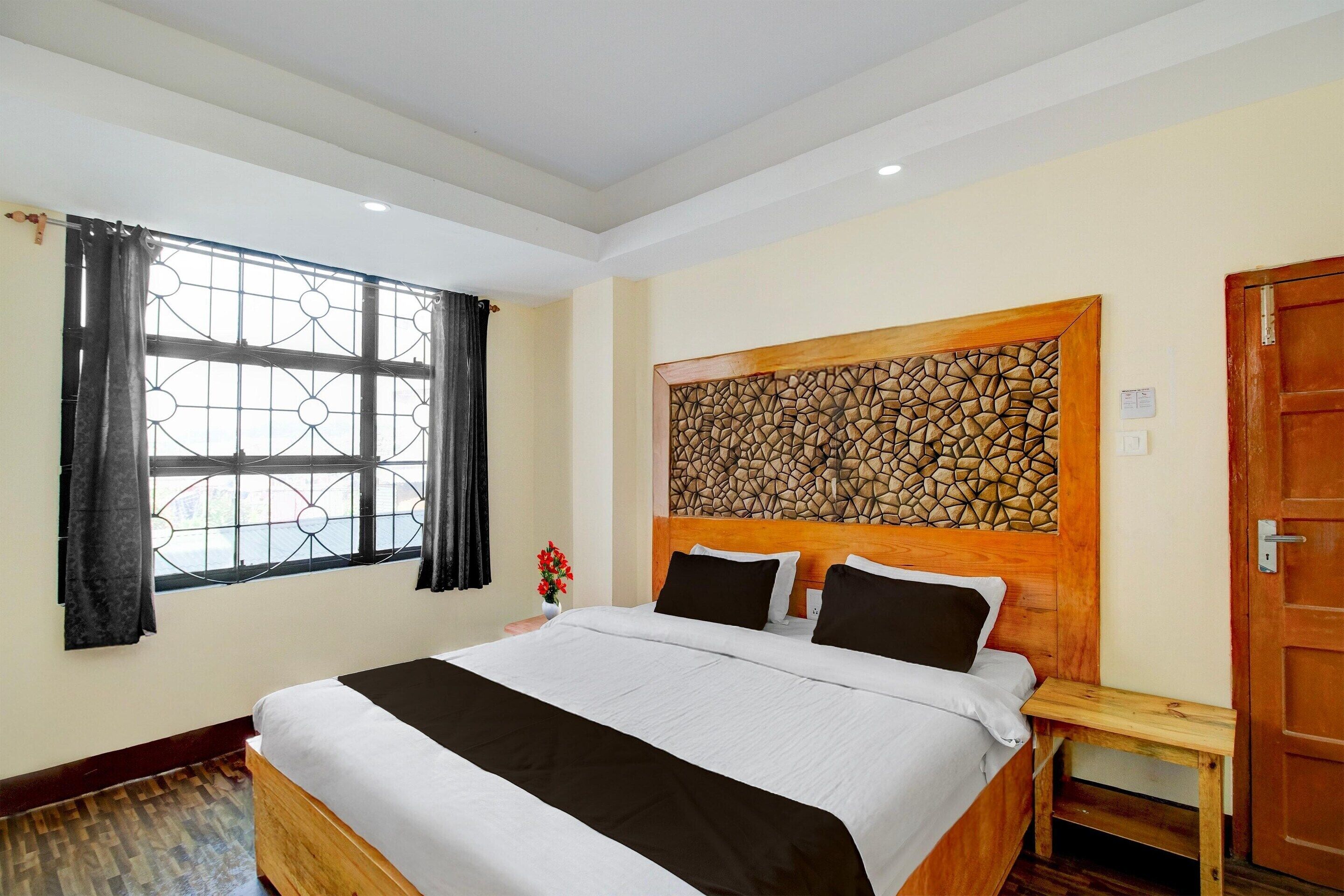 Een hotelkamer met een groot bed, een raam met gordijnen, een houten hoofdeinde en een deur.