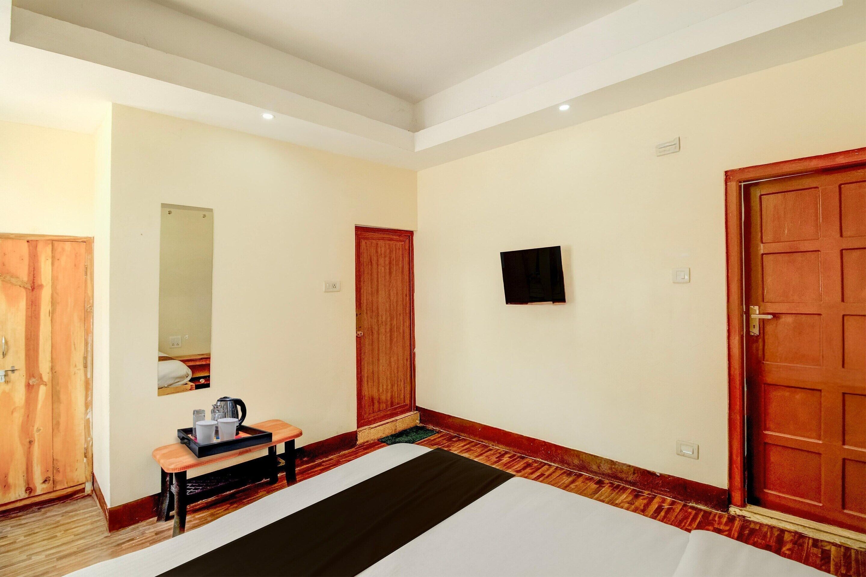 Habitación de hotel con cama, escritorio con hervidor, espejo, televisor y puerta de madera.