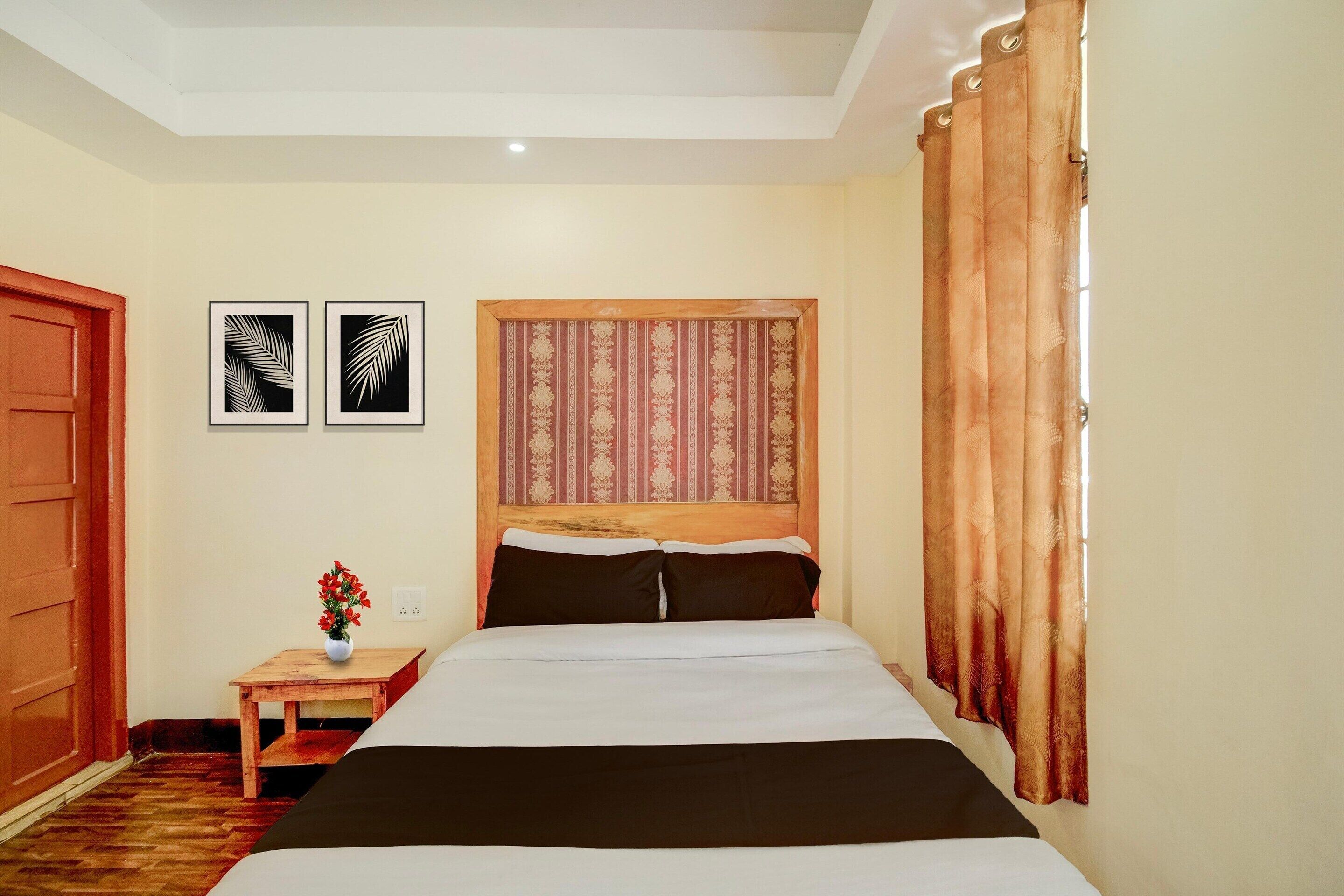 A hotel room with a bed, a nightstand, a vase with flowers, and two framed pictures on the wall.