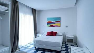 Une chambre d’hôtel avec un lit, un bureau, une chaise, une table de chevet, un tableau au mur et une fenêtre avec des rideaux.