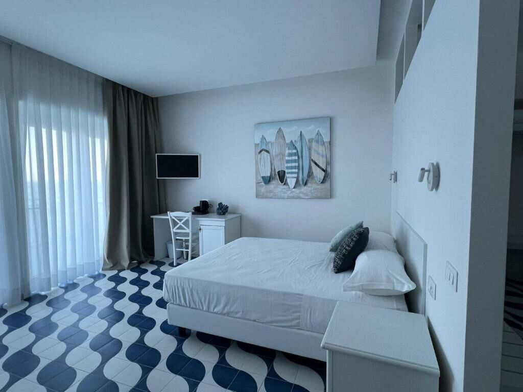 Una camera d'albergo con un letto, una scrivania, una sedia, una televisione e un quadro appeso al muro.
