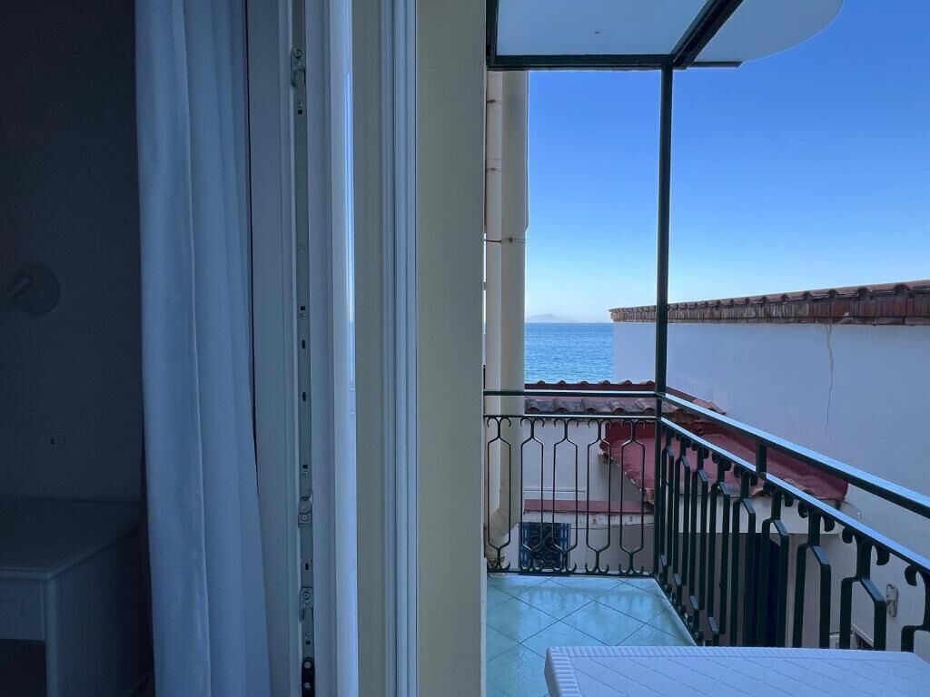 A balcony with a view of the sea, a tiled floor, and a metal railing.
