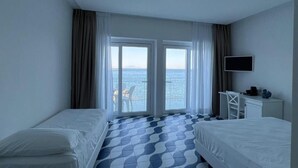 Habitación de hotel con dos camas, televisión, escritorio y vista al mar.