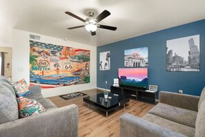 Un salon doté d’un ventilateur de plafond, d’une grande fresque représentant la Route 66, d’un téléviseur à écran plat et d’un tableau représentant un paysage urbain.