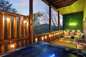A wooden deck with a hot tub, a sofa, and a wall with a green wall feature. - Bear’s Eye View - Sleeps 12, Hot Tub, Game Room & Mountain Views (Sevierville)