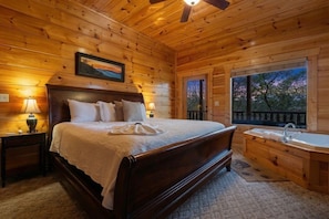 Ein Schlafzimmer in einer Holzhütte mit Bett, Nachttischlampen, einem Fenster und einer eingebauten Badewanne.