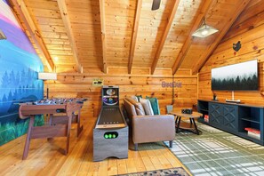 Ein Zimmer mit Holzboden, einem Kicker, einer Couch und einem Fernseher.