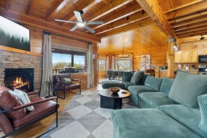 Ein rustikaler Innenraum einer Blockhütte mit Kamin, einem grünen Sofa, einem Essbereich und einer Küche.