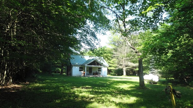 Une maison avec un porche, entourée d’arbres et d’herbe.