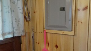 Une pièce aux murs lambrés, avec une grande porte grise, un rideau blanc orné de motifs floraux et un balai rose appuyé contre le mur.